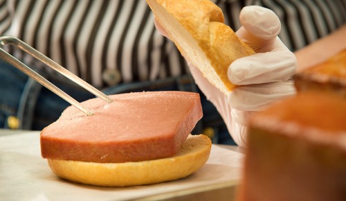 Feinkostmitarbeiter mit Leberkäsesemmel in der Früh