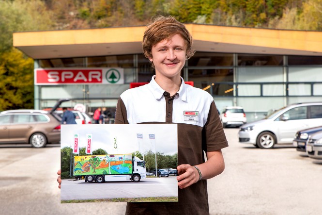 SPAR Lehrling vor Filiale mit Bild eines LKWs in der Hand