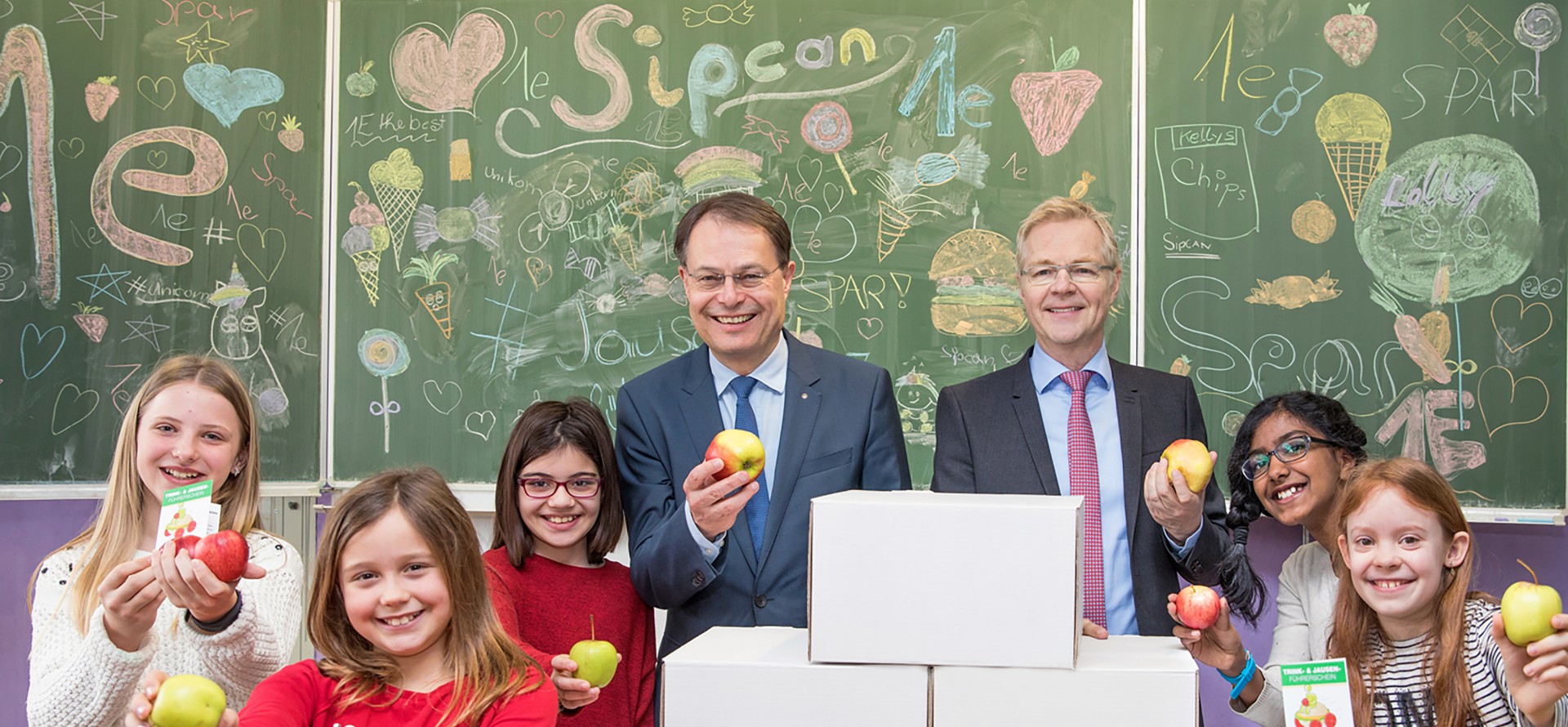 Schüler und Vorstandsvorsitzender Dr. Drexel mit gesunder Jause in Schulklasse vor Schultafel
