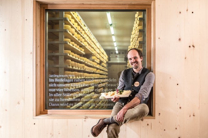 Michael Kerschbaumer  von Kaslabn sitzt mit selbst gemachtem Käse vor dem Reifelager