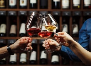 People in good mood clink glasses, celebrating together, photo focus on hands woman and man tasting degustation different types of wine, alcohol beverage to relax, bottles on shelves on background
