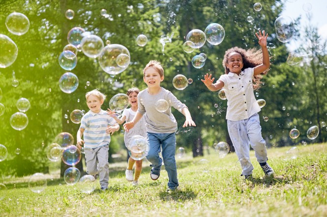 Little Kids Having Fun Outdoors Multi-ethnic group of little friends with toothy smiles on their faces enjoying warm sunny day while participating in soap bubbles show