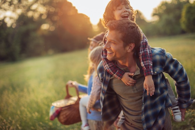 Picture of a young family going for a picnic, walking together threw high grass with the sun in their back.