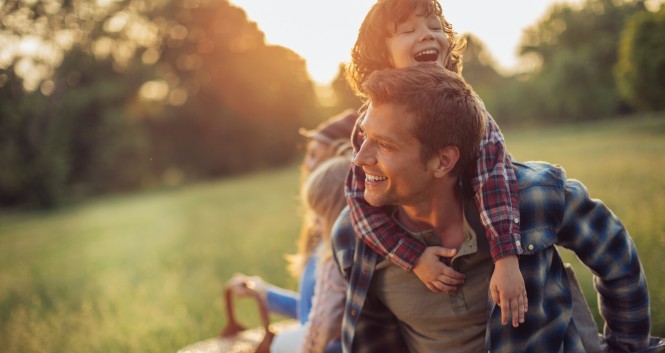 Picture of a young family going for a picnic, walking together threw high grass with the sun in their back.