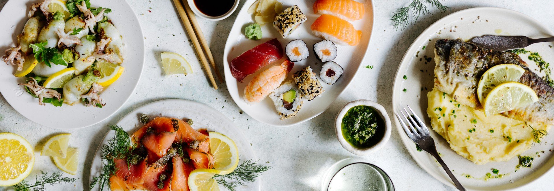 Beliebte Rezepte mit Fisch Ein Tisch mit beliebten Fisch-Rezepten: Sushi, Räucherlachs, gegrillte Calamari, Saibling mit Püree