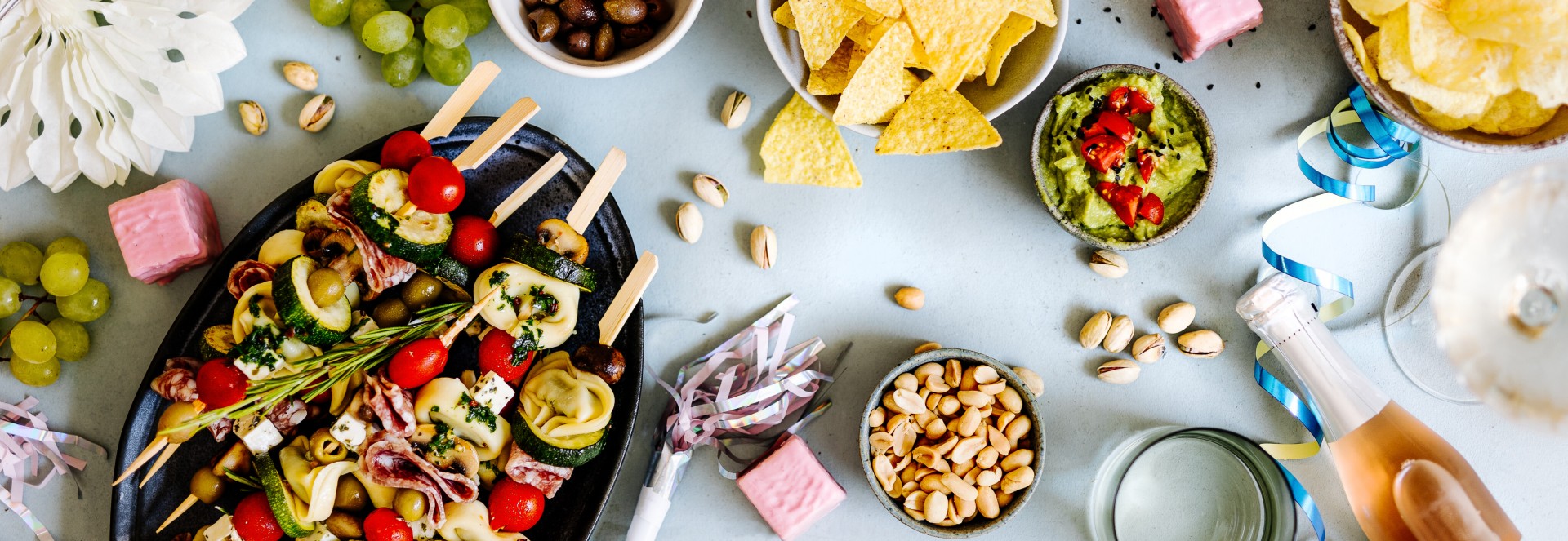 Partyrezepte Ein Tisch mit Partygerichten wie Antipasti-Spieße, Nachos, Guacamole