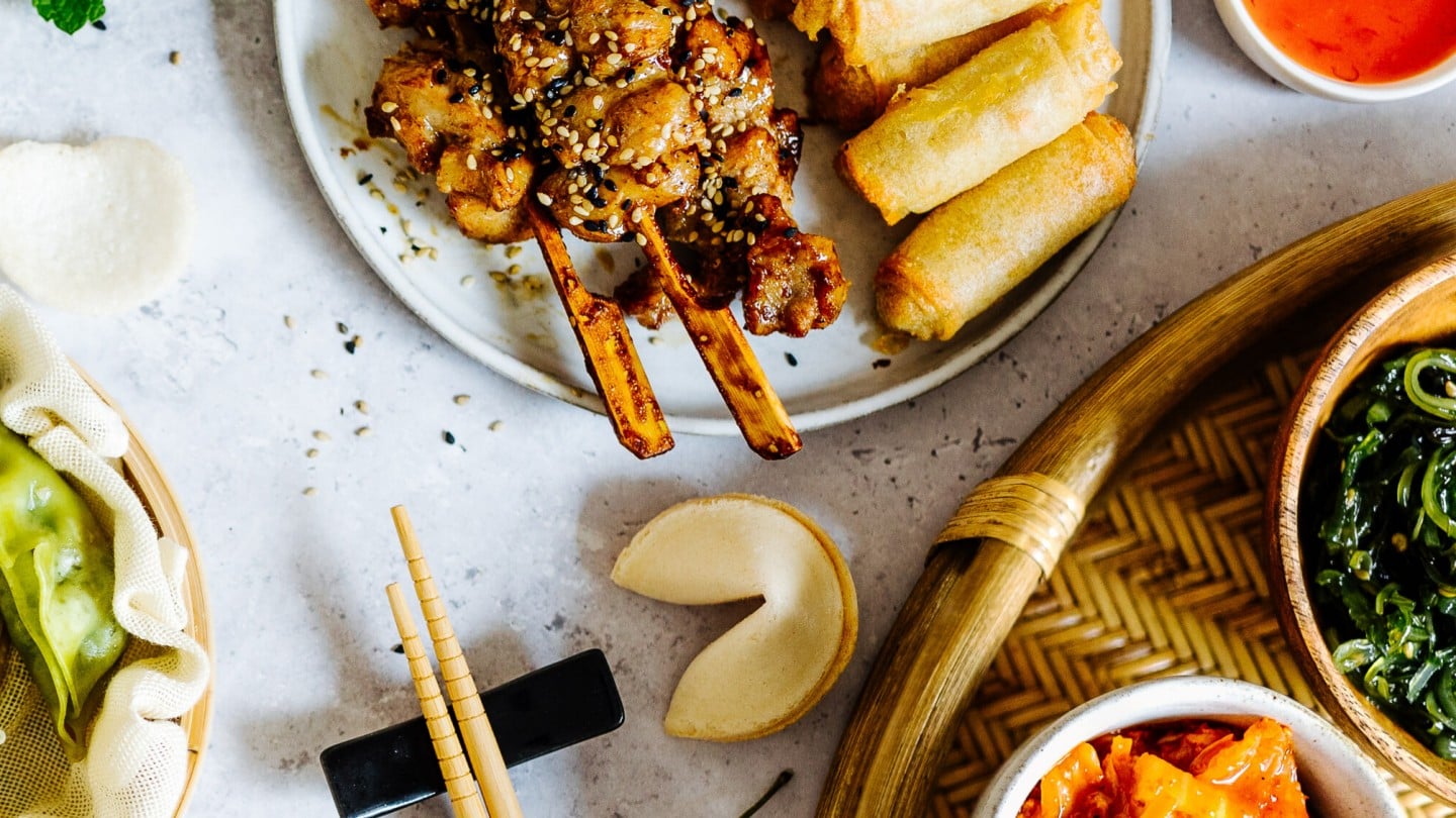 Ein Tisch gedeckt mit lauter asiatischen Gerichten, wie Sushi, Dumplings oder Frühlingsrollen