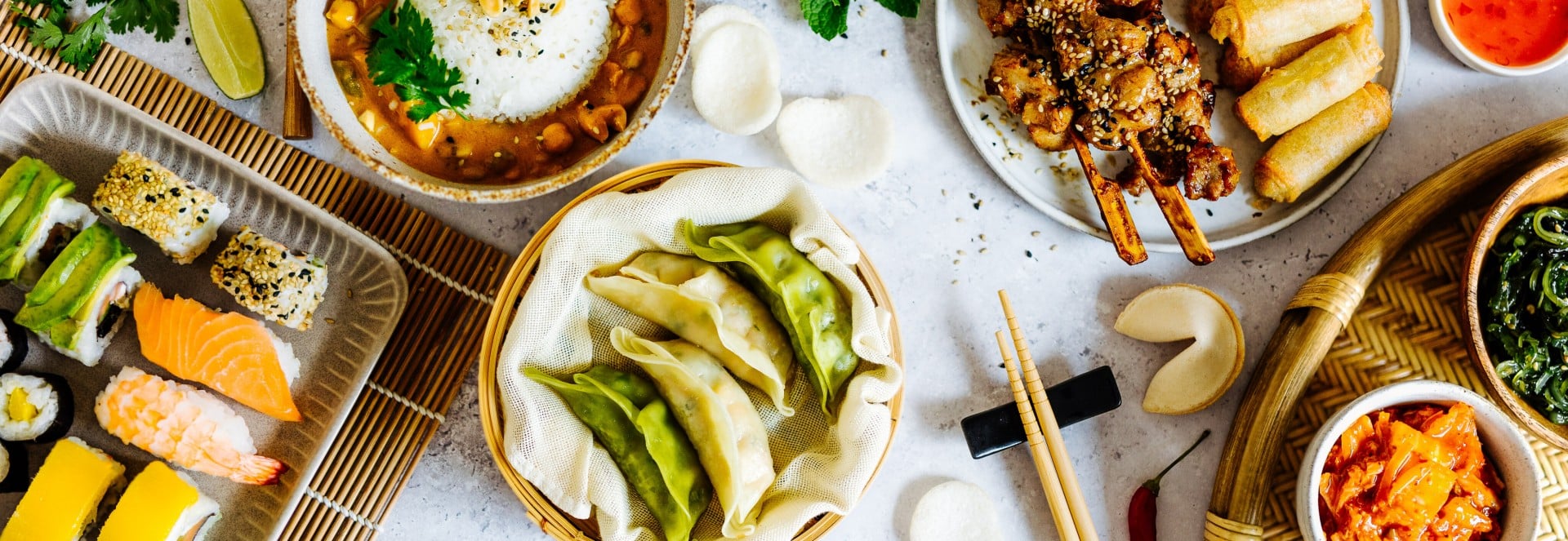 Ein Tisch gedeckt mit lauter asiatischen Gerichten, wie Sushi, Dumplings oder Frühlingsrollen