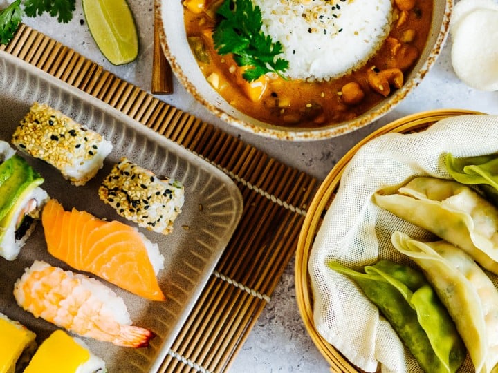 Ein Tisch gedeckt mit lauter asiatischen Gerichten, wie Sushi, Dumplings oder Frühlingsrollen