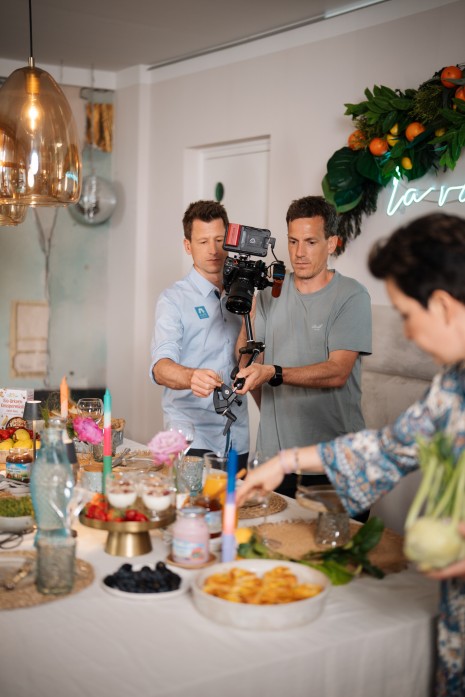 Behind the scenes, Kamermann filmt, Tici richtet den Tisch her und Hannes nähert sich im Hintergrund