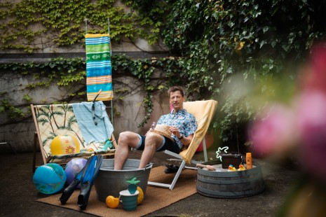 Hannes sitz in einem Hinterhof un einem Liegestuhl. Es sieht aus wie im Sommer am Strand