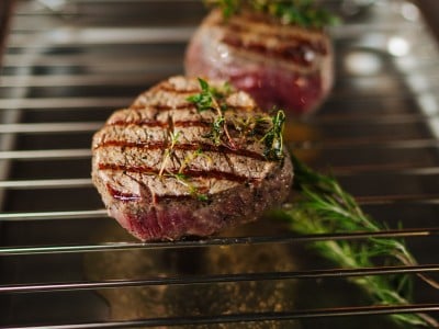 Das Steak gewürzt mit Thymian und Rosmarin liegt auf dem Backofenrost