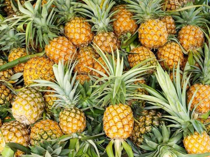 Foto einer tropischen Ananas als ganze Frucht mit grünen Blättern und gelber Schale, dargestellt als frisches, tropisches Obst auf neutralem Hintergrund.