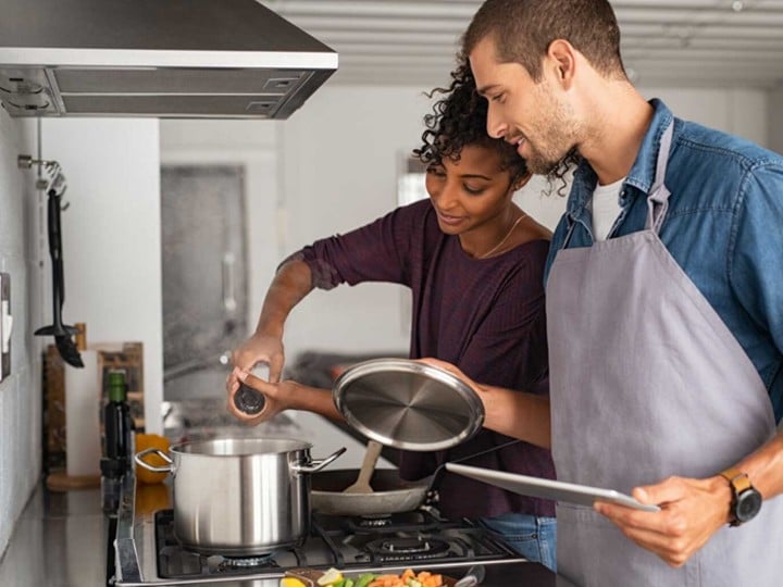 Frau und Mann kochen in einer Küche. Frau würzt das Gericht und der Mann schaut zu