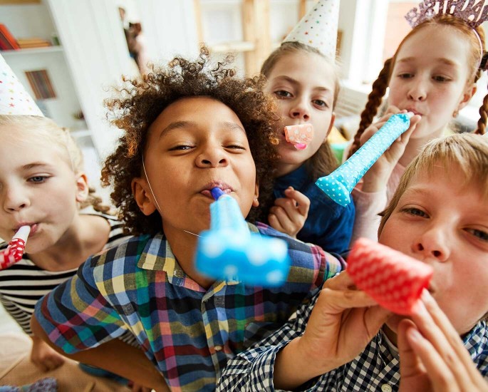 Viele Kinder tröten bei einer Kindergeburtstags-Party in das Bild
