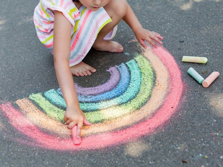 Mädchen malt mit Strassenkreide einen Regenbogen