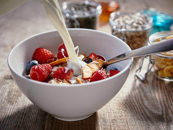 Eine Milchalternative wird ein eine Schale Müsli mit frischen Beeren gegossen