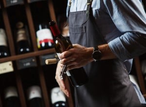 Sommelier holding bottle of red wine in cellar on background of shelves with elite alchoholic drinks, best choice in winemaking