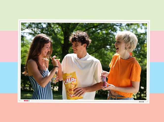 2 Frauen und ein Mann lächelnd im Sommer im Park mit einer Packung Chips und Getränken in der Hand