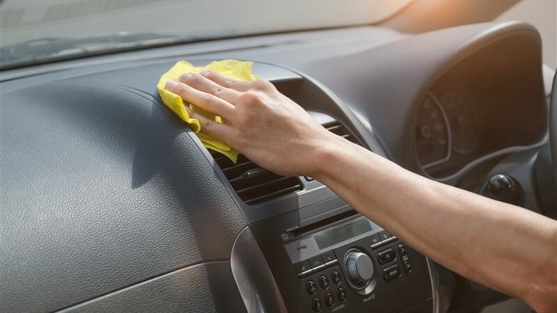 Person clean with wipe napkin the dashboard of the car in the sunlight 