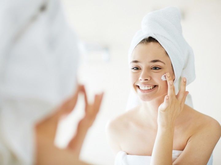 Young woman applying facial cream in front of mirror