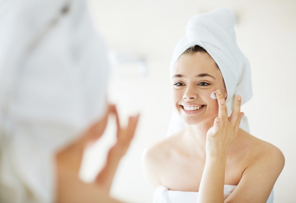 Young woman applying facial cream in front of mirror