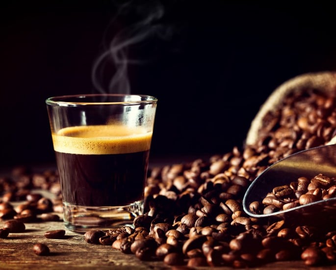 Espresso in einem Glas, daneben Kaffeebohnen