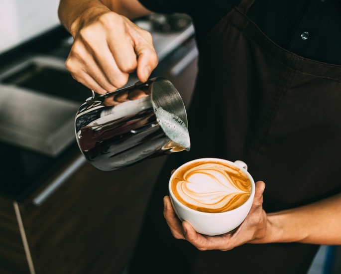 Ausschnitt eines jungen männlichen Baristas, der heiße Milch in heißen Espresso gießt