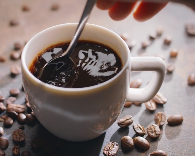 Tasse Americano-Kaffee und geröstete Kaffeebohnen neben der Tasse auf einem Holztisch. Ansicht von oben.