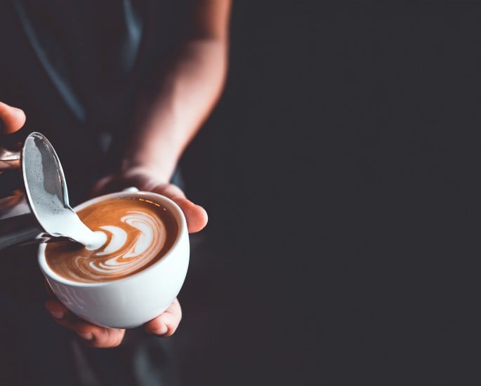 Vintage-Ton von Barista beim Eingießen von Milch zur Zubereitung von Latte-Art-Kaffee in einem Café oder einer Kaffeebar