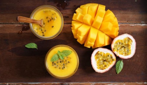 eine aufgeschnittene Mango und eine halbierte Maracuja auf einem Holztisch