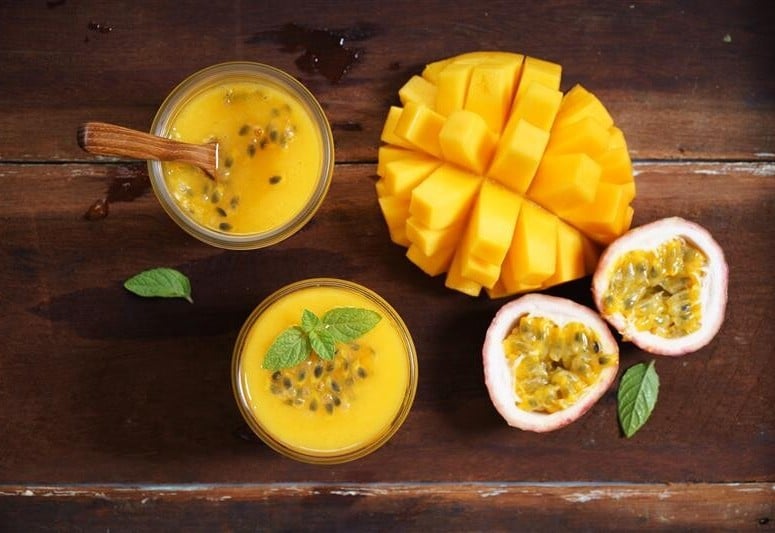 eine aufgeschnittene Mango und eine halbierte Maracuja auf einem Holztisch