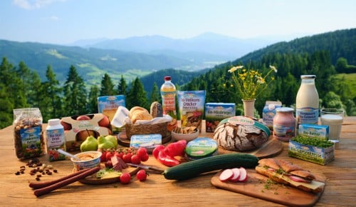Bio-Produkte von SPAR Natur pur auf einem Holztisch; im Hintergrund eine schöne Berglandschaft