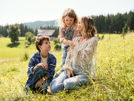 Mirjam Weichselbraun sitzt mit zwei Kindern in der Natur und betrachtet einen Schmetterling auf ihrer Hand