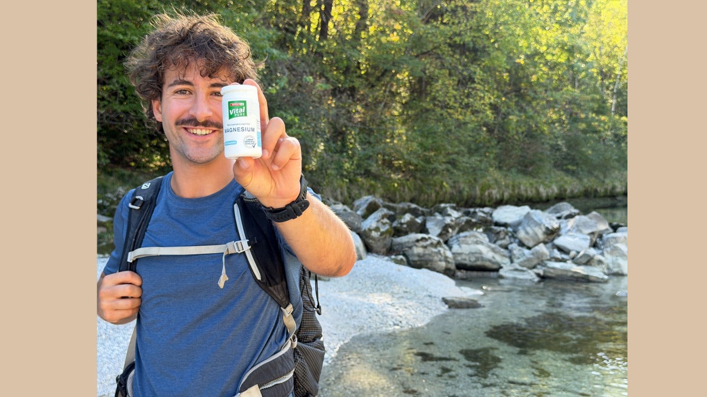 ein junger Mann lächelt zufrieden und hält eine Packung SPAR Vital PURE Magnesium in die Kamera
