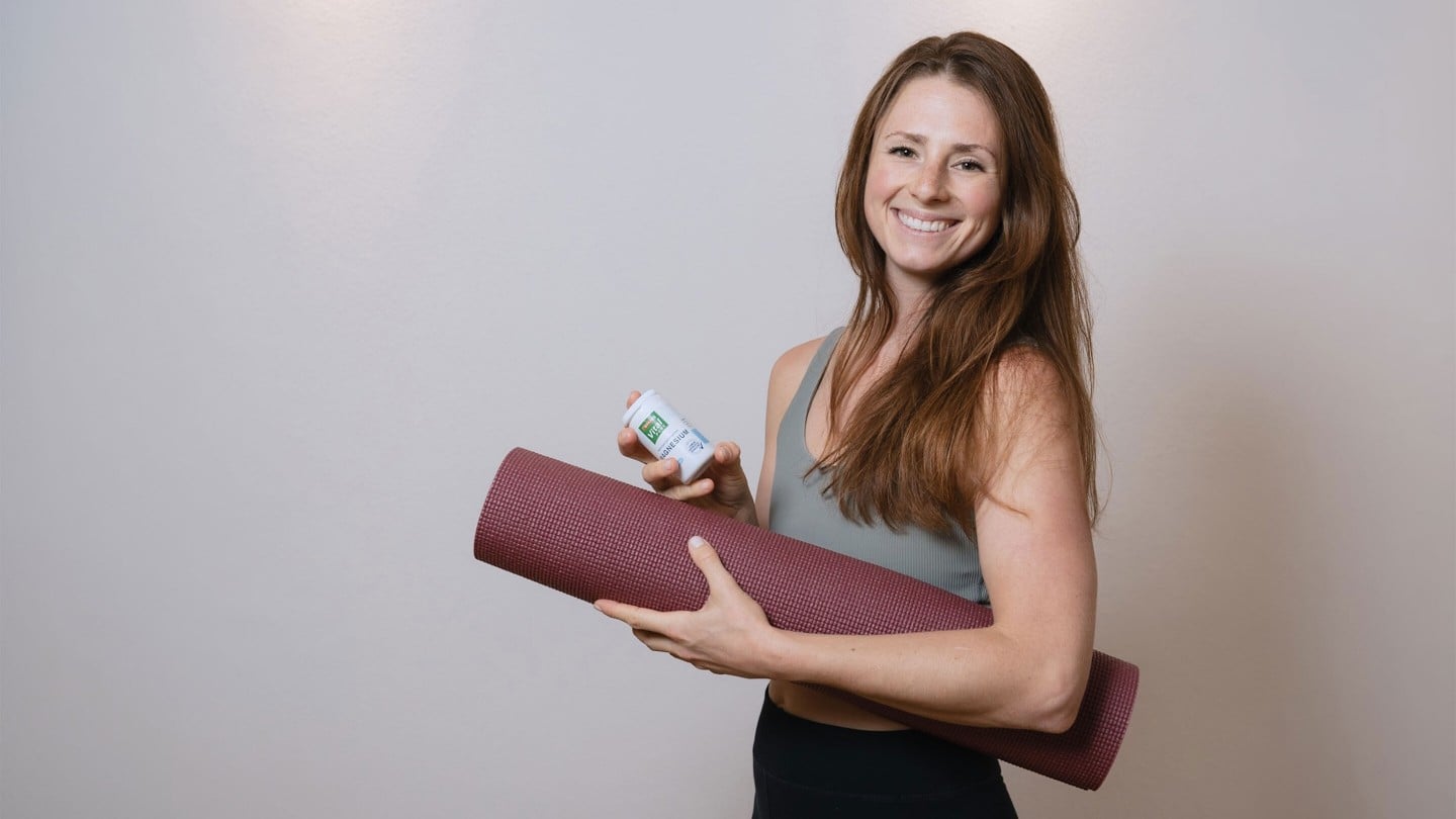 eine Frau hält eine Pilatesmatte im Arm und lächelt glücklich in die Kamera