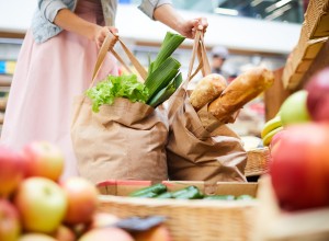 Close-up of unrecognizable woman in skirt standing in food organic store and picking heavy shopping bags full of products
