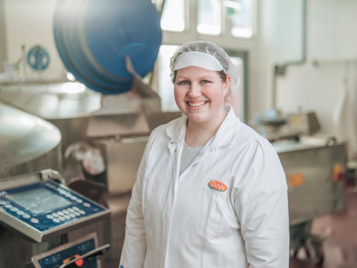 Mitarbeiterin in Hygienekleidung lächelt in Produktionsumgebung