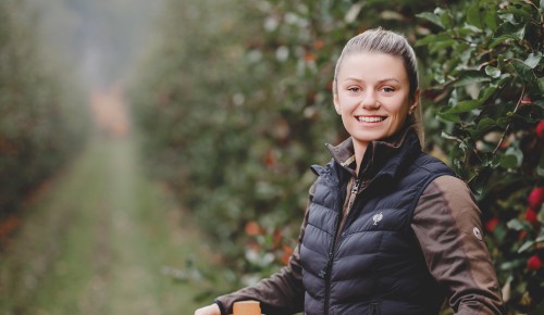 Lisa Brandl mit einer Holzkiste voll mit Äpfeln in einem Apfelgarten mit Herbststimmung