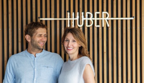 Markus und Edith Huber vor einer Holzwand mit Huber als Leuchtschrift