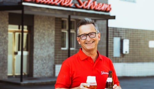 Karl Theodor Trojan vor der Brauerei Schrems mit einer Bierflasche und einem gefüllten Bierglas in den Händen