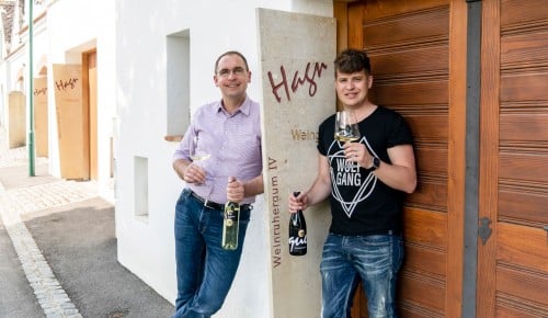 Leo und Wolfgang Hagn vor dem Weinruheraum des Weinguts mit jeweils einer Flasche Wein und einem Weinglas