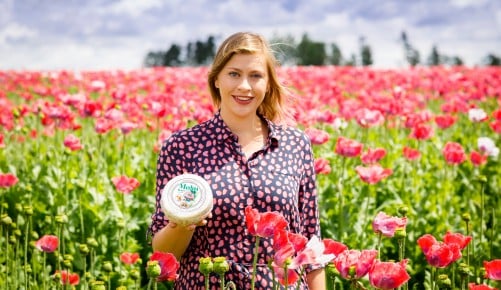 Geschäftsführerin Doris Ploner mitten in einem Mohnfeld mit einem Käse in der Hand an einem sonnigen Tag