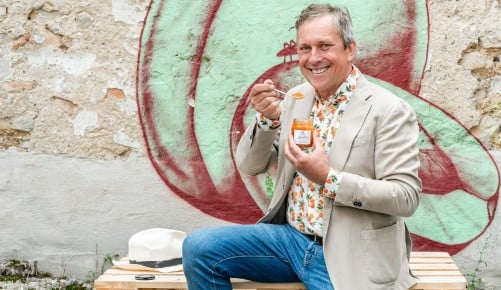 Stefan Schauer von der Firma Stauds sitzt auf einem Stapel Paletten und hält eine Marillenmarmelade in der Hand