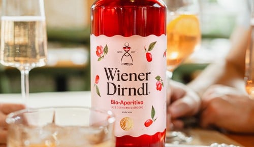 Wiener Dirndl Aperitivo Flasche im Fokus auf einem Tisch im Hintergrund verschwommene Hände und Gläser