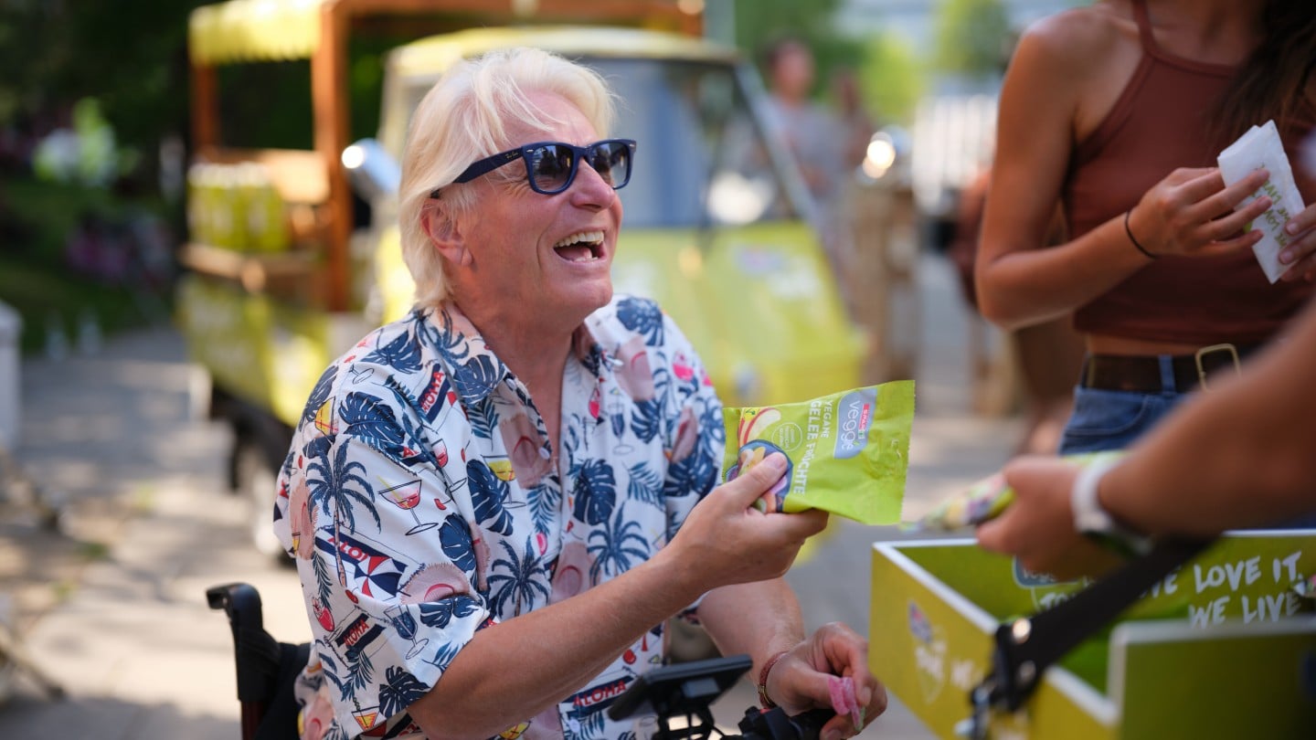 Lachender Mann im Rollstuhl hält SPAR Veggie Gelee Früchte in der Hand. 