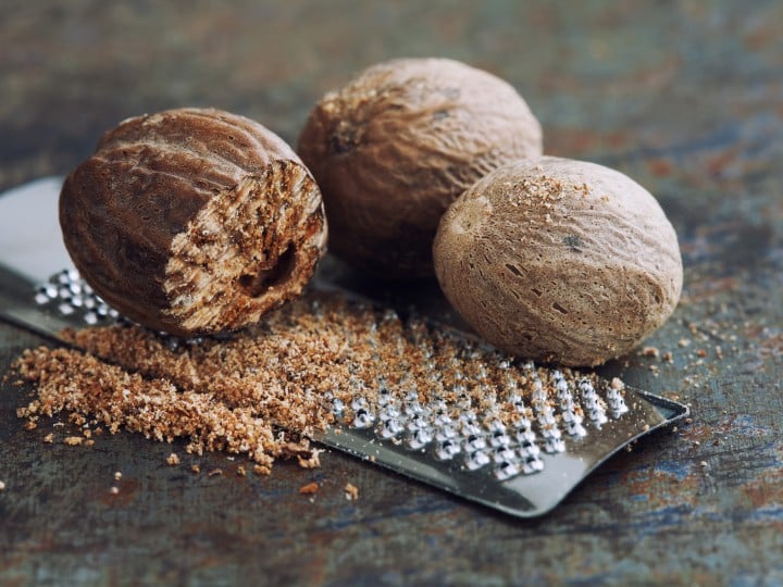 Making nutmeg powder. Macro view silver grater with grated muscat nuts. Kitchen still life photo. Shallow depth of field, retro rusty background. Selective focus.