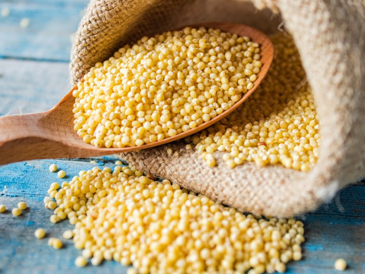 Raw yellow millet in a wooden spoon on burlap cloth on a background of blue rustic boards. Close-up.