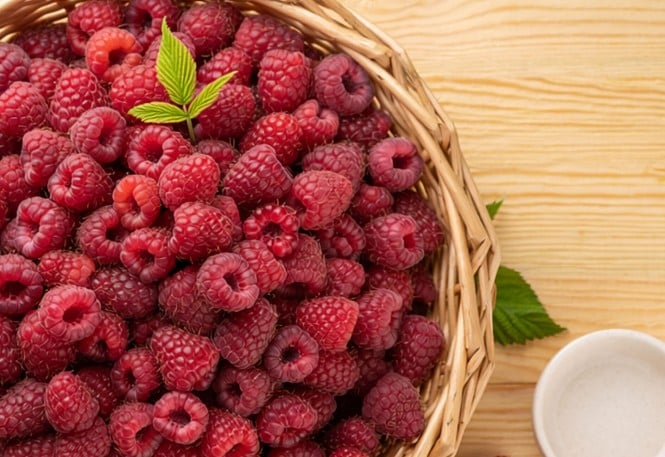 Hier sieht man einen Korb von oben der auf einem Tisch steht und voll gefüllt ist mit reifen prallroten Himbeeren