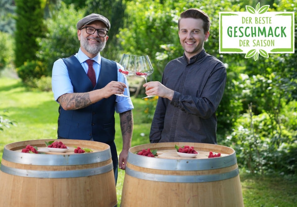Hier sieht man zwei Sommeliers die sich gegenseitig mit zwei Weingläsern die mit Himbeeren gefüllt sind zuprosten